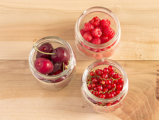 Glass jars with different fruit (redcurrant, raspberry and cherries) on a wooden table