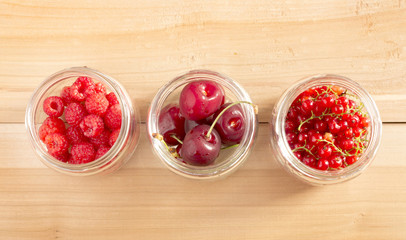 Glass jars with different fruit (redcurrant, raspberry and cherries) on a wooden table