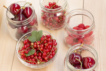 Glass jars with different fruit (redcurrant, raspberry and cherries) on a wooden table
