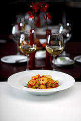 Shrimps, rice and vegetables served at the table with wine glasses in the background