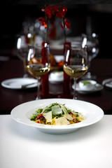 Pasta with arugula and parmesan with glass of white wine in background, shallow depth of field