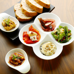 Mixed food on a white and a black plate with ham, yellow dressing, chicken in spicy sauce with sesame seeds and paprika on which pieces of cheese, mint and parsley