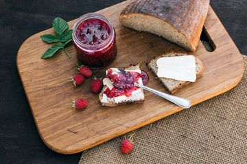 Raspberry jam and bread with butter in a jar on the wooden table Lunch breakfast