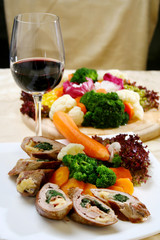 Rolled meat stuffed with vegetables and cooked vegetables on the side and glass of red wine