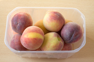 Peaches in transparent plastic container on wooden background
