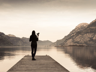 Fototapeta premium Photographer. The female figure with a camera in hand on a wooden pier. 