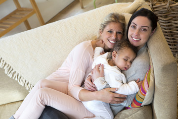 Fototapeta premium Same sex female couple cuddling on the sofa with their sleeping son