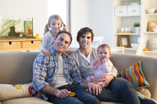 Same sex male couple smiling for the camera with their daughters at home.