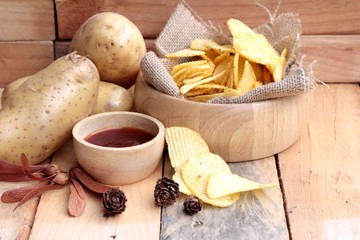 Potato chip and fresh potatoes on wood background