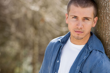 Close up shot of an attractive young man leaning against a tree outdoors