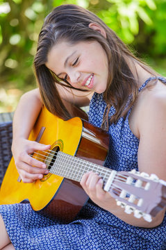 Portrait of very cute teenager playing guitar in her garden