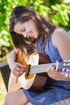 Portrait of very cute teenager playing guitar in her garden