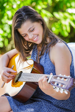 Portrait of very cute teenager playing guitar in her garden