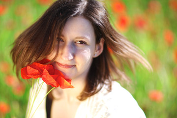 Naklejka premium Young atractive woman standing among blooming poppies on a sunny day