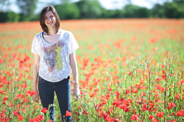 Young atractive woman standing among blooming poppies on a sunny day