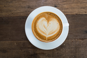 A cup of coffee with heart pattern in a white cup on wooden background