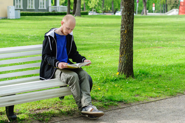 Young man reads on a bench in park
