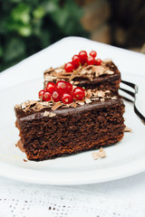 Two brownies with redberries on top, served in a plate on a wooden table
