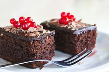 Two brownies with redberries on top, served in a plate on a wooden table
