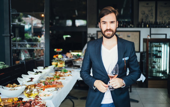 Young elegant man standing in the restaurant, holding a glass of wine. Man's style