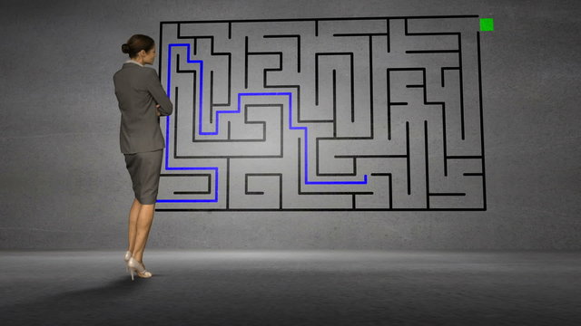 Businesswoman looking at grey wall with maze