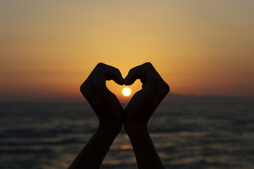 heart shape silhouette made with hands against sunset