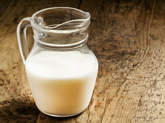 Jug of milk on old wooden table in rustic style, selective focus