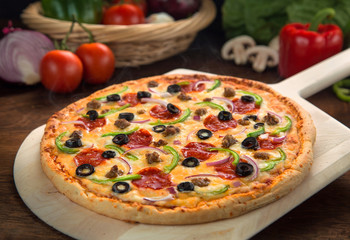 Entire supreme pizza baked cooked fresh and hot from oven served on wood surface