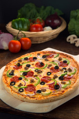 Vertical shot of Delicious full supreme deluxe pizza baked fresh out of the oven next to ingredients