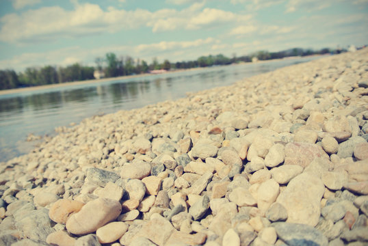 Pebbly Lake Shore On A Sunny Summer Afternoon, Filtered In Faded, Washed Out, Retro Style; Nostalgic Summer Vintage Concept. Low Angle Perspective.