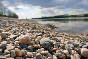 Closeup of yellow and white pebbles on the lake shore on a sunny summer afternoon with dramatic sky; low angle shot. Personal pov.