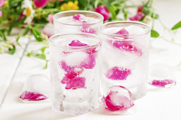 Fresh sparkling beverage with ice with rose petals on white wood