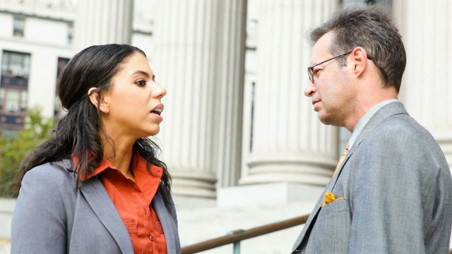 Professionally dressed man and woman having a conversation outdoors on the steps of a building with columns. Could be lawyers,  lawyer and client, or business people.