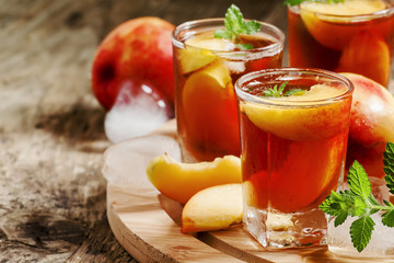 Ice Peach Tea with pieces of fruit, ice and mint on a wooden boa