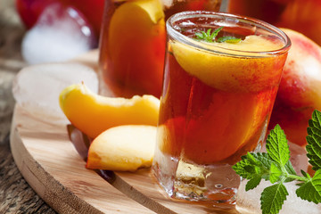 Ice Peach Tea with pieces of fruit, ice and mint on a wooden boa