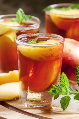 Ice Peach Tea with pieces of fruit, ice and mint on a wooden boa