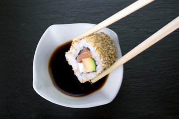 piece of sushi dipping in soy sauce / macro of Sushi roll in chopsticks dipped in soy sauce 