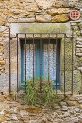 Old blue window closed and covered by rusty metal jail on a rock wall