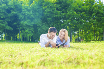 Happy Caucasian Couple in Love Lying on the Grass Outdoors. Read
