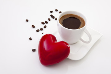 Coffee cup with saucer and scattered beans and big red heart on the left shot front on at an angle on a white background
