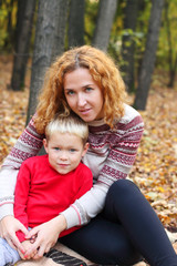 Fototapeta na wymiar Young mother with happy son in red sit in yellow autumn forest