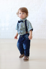 Little handsome curly boy in jeans stands in room 