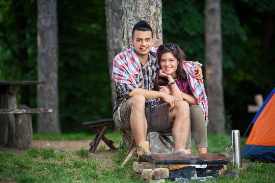 Young couple wrapped in blanket warming up by the fire in front of the tent