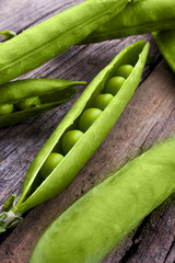 Peas in a pod shot at an angle from above on a wooden background portrait
