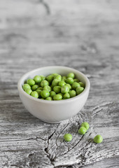 green peas in a white bowl on a light wooden background