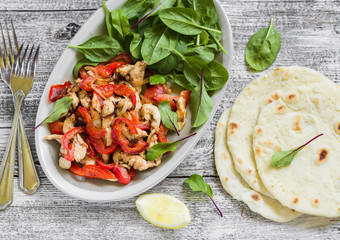 stir fry with chicken breast, red peppers and onions, fresh spinach and homemade tortilla on a light wooden background