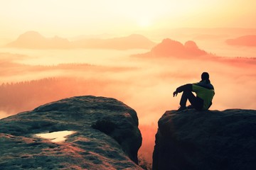 Rear view of male hiker sitting on the rocky peak  while enjoying a colorful daybreak above...