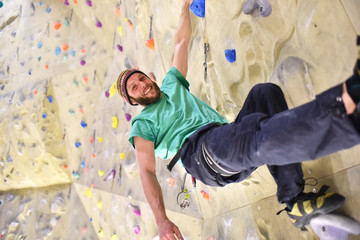 glücklicher Sportler in einer Kletterhalle // 
climber hanging on a wall and smiling