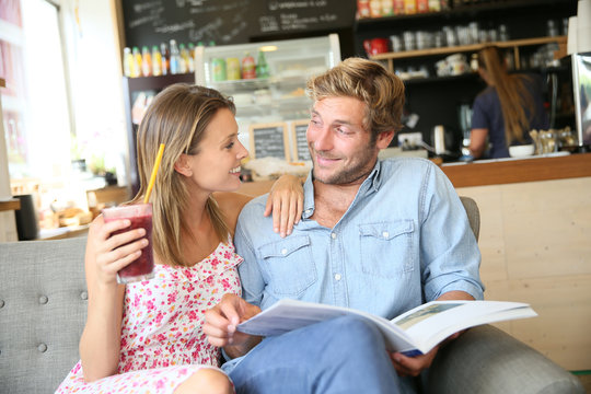 Trendy couple in coffee shop reading magazine sitting in sofa