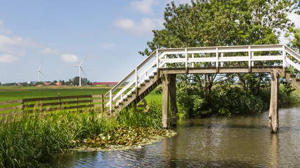 Fototapeta na wymiar Typical Dutch landscape with an old wooden bridge and modern win